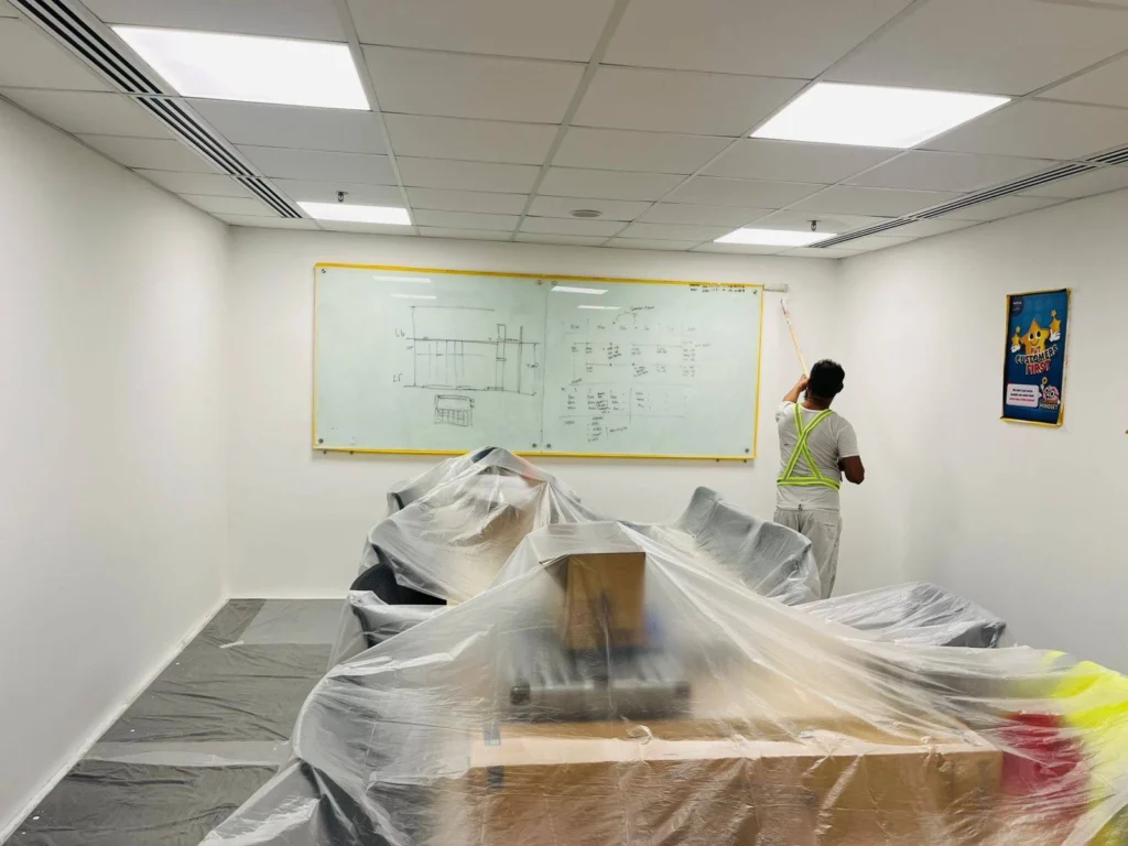 Commercial office interior painting Singapore – painter rolling conference room wall beside whiteboard